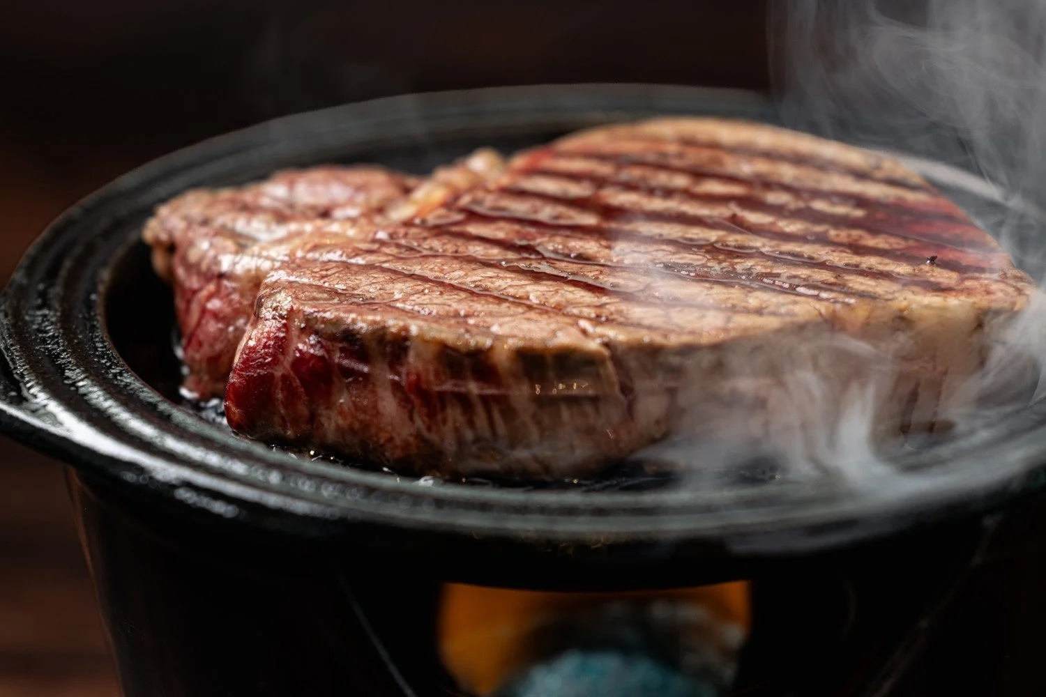 熱々の鉄板の上で、美しい焼き目がついた厚切りのステーキが湯気を立てながら焼かれている