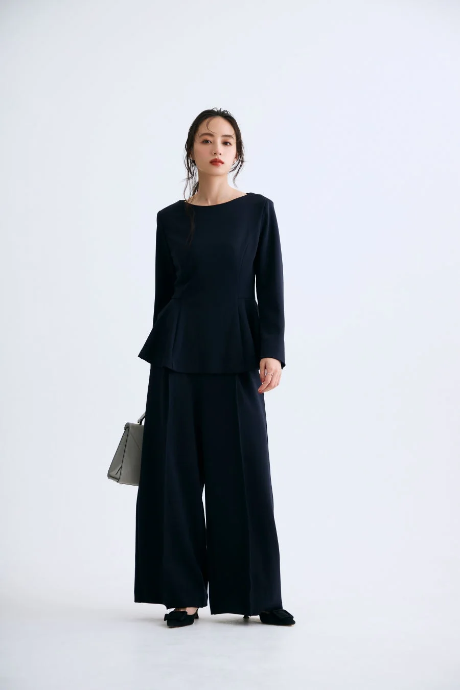 ネイビーのペプラムトップスとワイドパンツのセットアップを着用した女性モデル